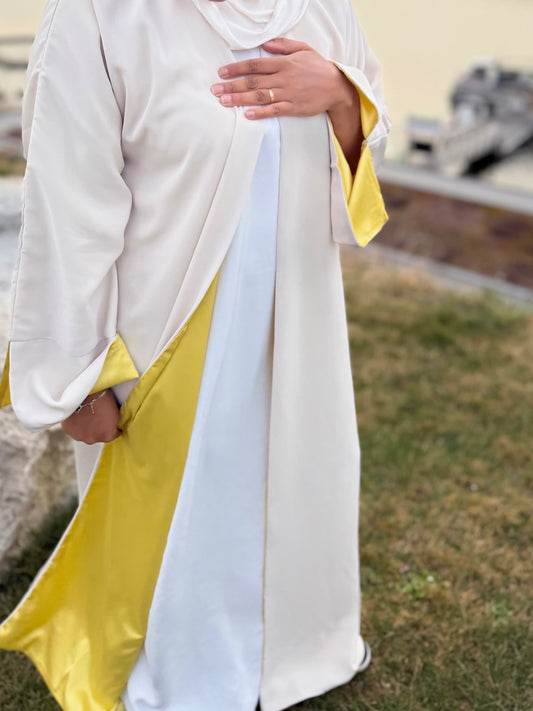 Abaya longue crème avec revers satin jaune vue trois quarts tissu fluide soyeux cérémonie femme - Naqî Collection