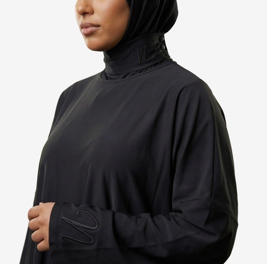 Femme portant un burkini 3 pièces noir avec cagoule intégrée - coupe ample et confortable - zoom sur les détails de la cagoule et du tissu ainsi que le logo